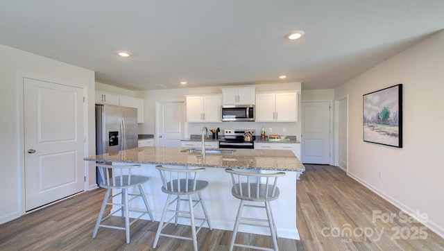 kitchen featuring sink, light wood-type flooring, white cabinetry, an island with sink, and stainless steel appliances