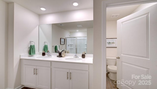 bathroom with hardwood / wood-style floors, toilet, a shower with shower door, and vanity