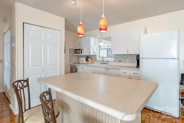 kitchen featuring decorative light fixtures, white cabinetry, sink, a center island, and white appliances