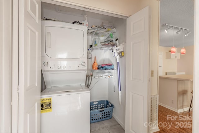 laundry area featuring light tile patterned floors, rail lighting, a textured ceiling, and stacked washing maching and dryer