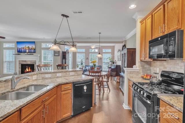 kitchen featuring ceiling fan, a stone fireplace, black appliances, a sink, and crown molding