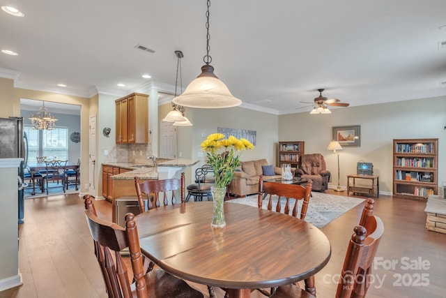 dining space featuring visible vents, light wood-style flooring, recessed lighting, ornamental molding, and ceiling fan with notable chandelier