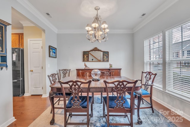 dining area with a notable chandelier, light wood-style floors, visible vents, and ornamental molding