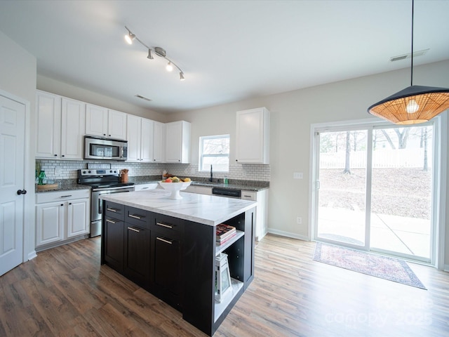 kitchen with appliances with stainless steel finishes, decorative light fixtures, sink, white cabinets, and a center island