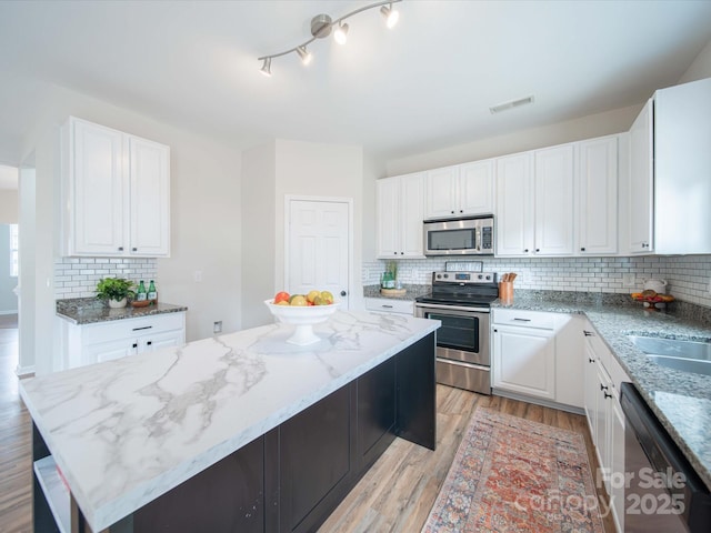 kitchen with stainless steel appliances, a center island, white cabinets, and light stone counters