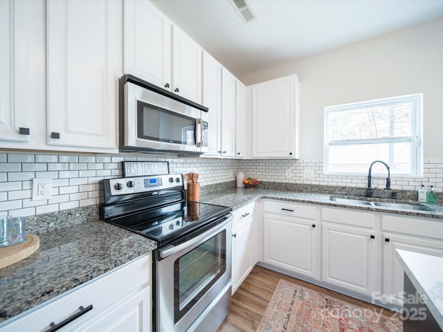 kitchen featuring white cabinetry, stainless steel appliances, sink, and dark stone countertops