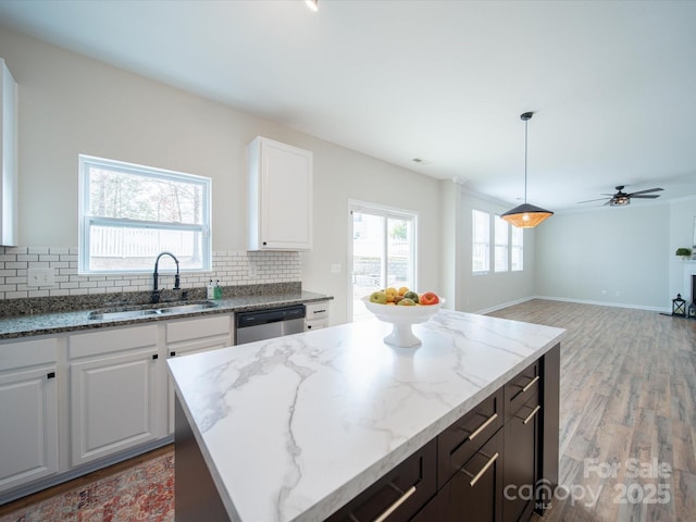 kitchen featuring a kitchen island, sink, white cabinets, stainless steel dishwasher, and light stone counters