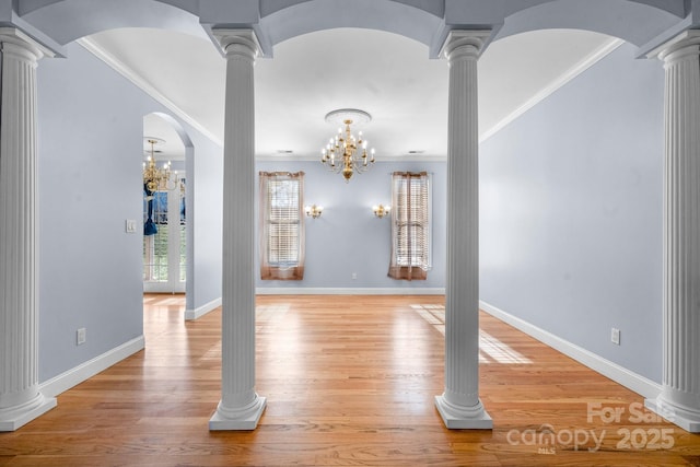 spare room featuring ornate columns, ornamental molding, a notable chandelier, and light hardwood / wood-style floors