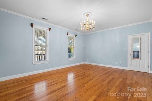 empty room featuring wood-type flooring, ornamental molding, and a notable chandelier