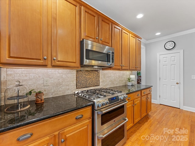 kitchen featuring crown molding, tasteful backsplash, light hardwood / wood-style flooring, appliances with stainless steel finishes, and dark stone counters