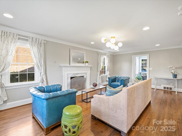 living room with wood-type flooring, ornamental molding, an inviting chandelier, and a premium fireplace