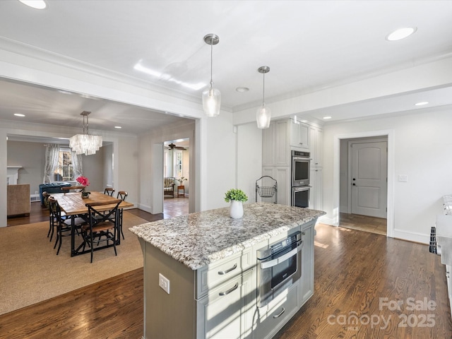 kitchen with double oven, decorative light fixtures, dark wood-type flooring, light stone counters, and a center island