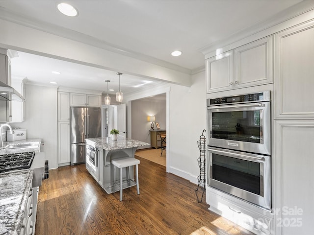 kitchen featuring appliances with stainless steel finishes, hanging light fixtures, a kitchen breakfast bar, a kitchen island, and light stone counters