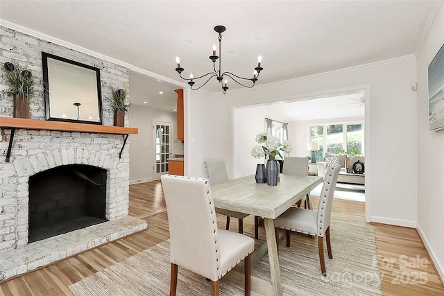 dining room featuring crown molding, an inviting chandelier, light wood-type flooring, a brick fireplace, and baseboards