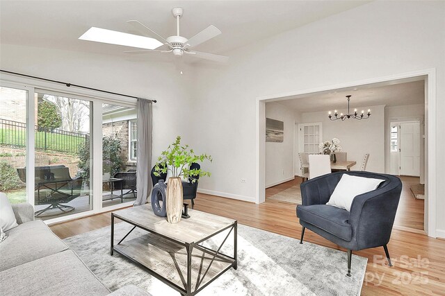living area featuring ceiling fan with notable chandelier, light wood finished floors, baseboards, and lofted ceiling