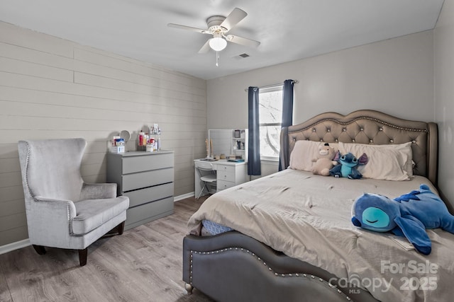 bedroom featuring wooden walls, ceiling fan, and light hardwood / wood-style floors