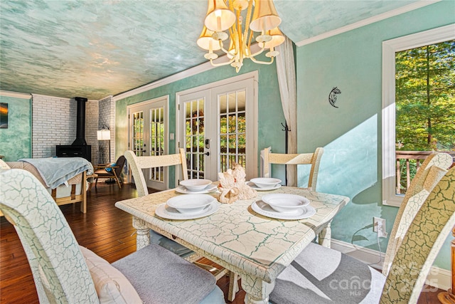 dining space with wood-type flooring, a wood stove, ornamental molding, a chandelier, and french doors