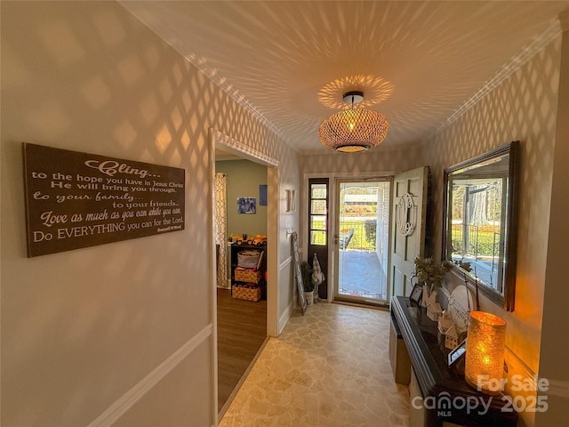 entryway with stone finish floor, wallpapered walls, baseboards, and crown molding