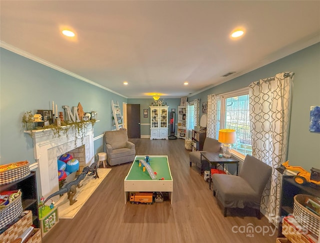 rec room featuring recessed lighting, visible vents, a fireplace with flush hearth, ornamental molding, and wood finished floors