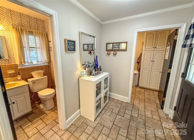 interior space featuring a sink, tile walls, baseboards, stone finish floor, and crown molding