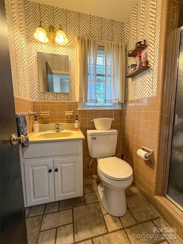 bathroom featuring tile walls, stone tile flooring, toilet, a shower stall, and vanity