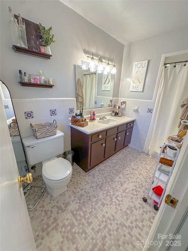 full bath featuring toilet, a wainscoted wall, tile patterned floors, vanity, and tile walls