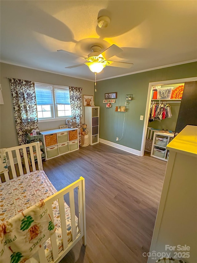 bedroom featuring wood finished floors, a ceiling fan, baseboards, ornamental molding, and a closet