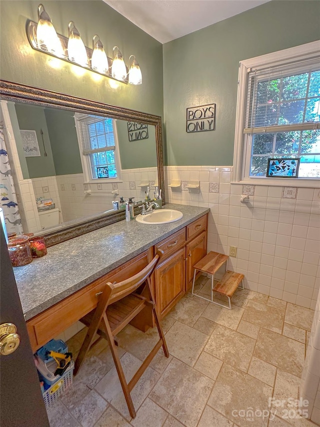 bathroom with stone tile flooring, wainscoting, tile walls, and vanity