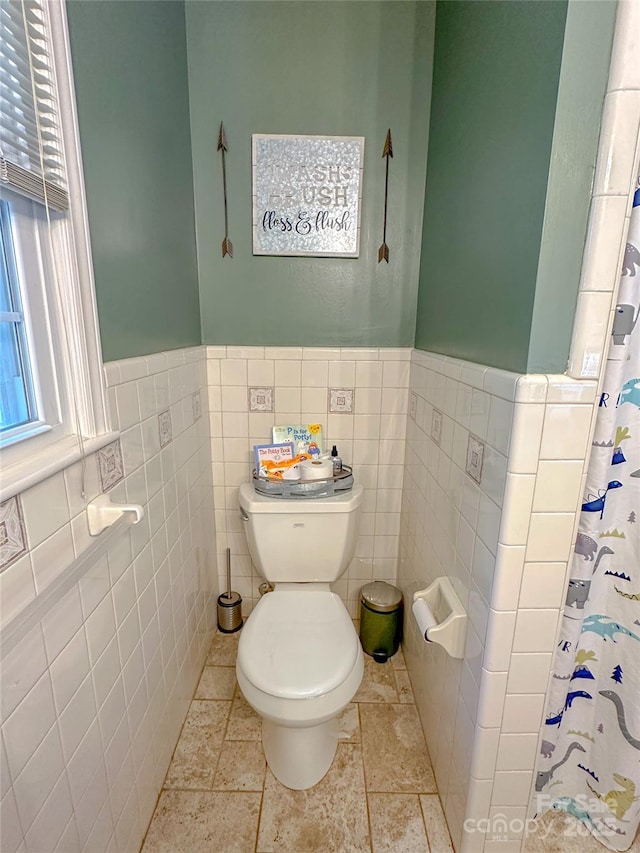 bathroom featuring toilet, a wainscoted wall, tile walls, and a shower with shower curtain