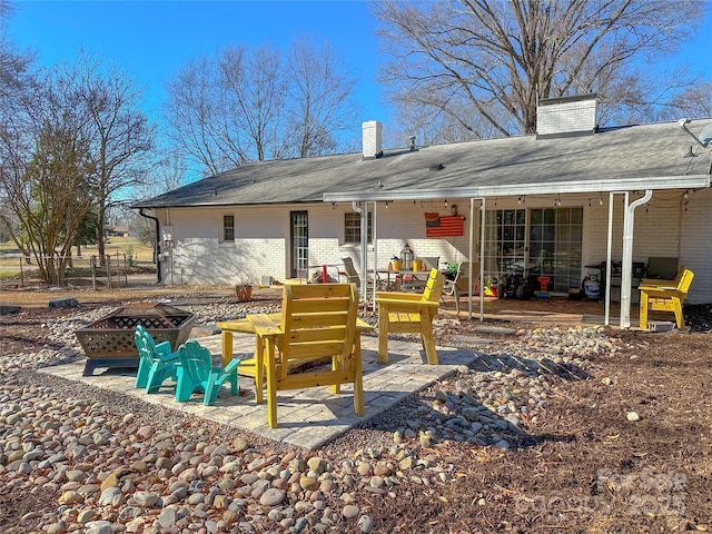 rear view of property with a fire pit, a patio, brick siding, and a chimney