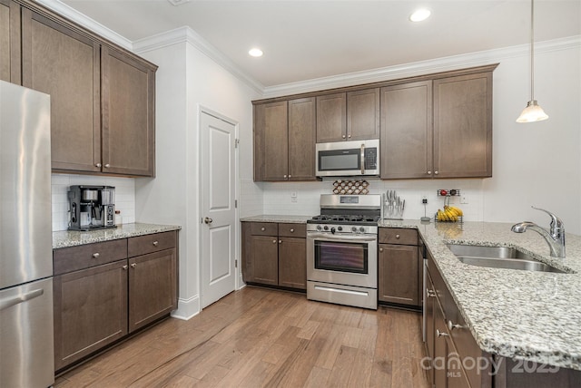 kitchen with pendant lighting, sink, appliances with stainless steel finishes, light stone countertops, and light hardwood / wood-style floors