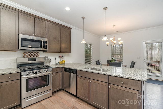 kitchen with decorative light fixtures, sink, light stone counters, kitchen peninsula, and stainless steel appliances