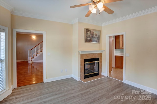 unfurnished living room with a tiled fireplace, light hardwood / wood-style flooring, ceiling fan, and ornamental molding