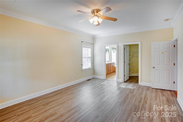 unfurnished bedroom with crown molding, ceiling fan, ensuite bath, a walk in closet, and a closet