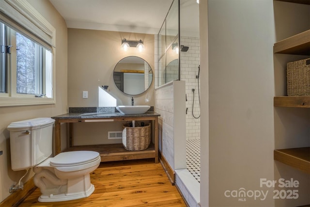 bathroom with sink, toilet, a tile shower, and wood-type flooring