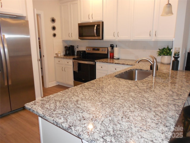 kitchen with tasteful backsplash, a peninsula, stainless steel appliances, white cabinetry, and a sink