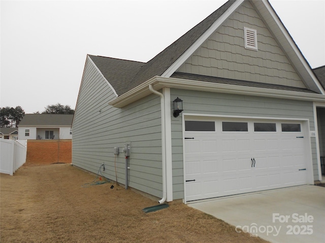 view of property exterior with driveway, an attached garage, fence, and a shingled roof