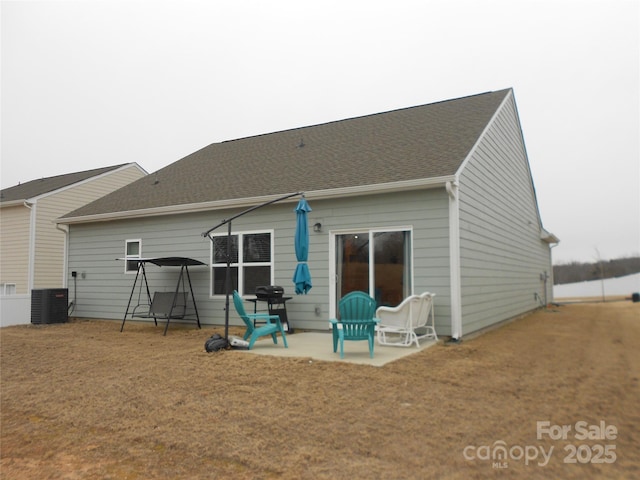 back of property with central AC, roof with shingles, and a patio area