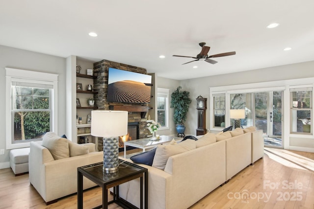 living room with a stone fireplace, light hardwood / wood-style flooring, and ceiling fan