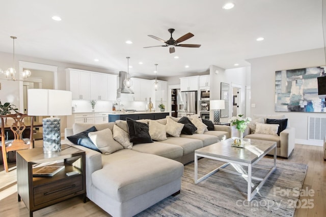 living room with ceiling fan with notable chandelier and light hardwood / wood-style floors