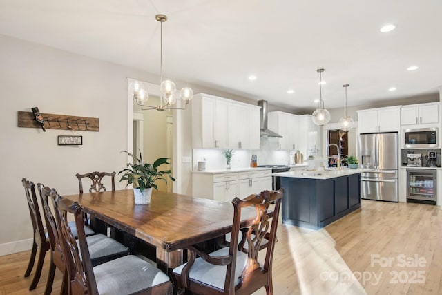 dining area with sink, a chandelier, beverage cooler, and light wood-type flooring