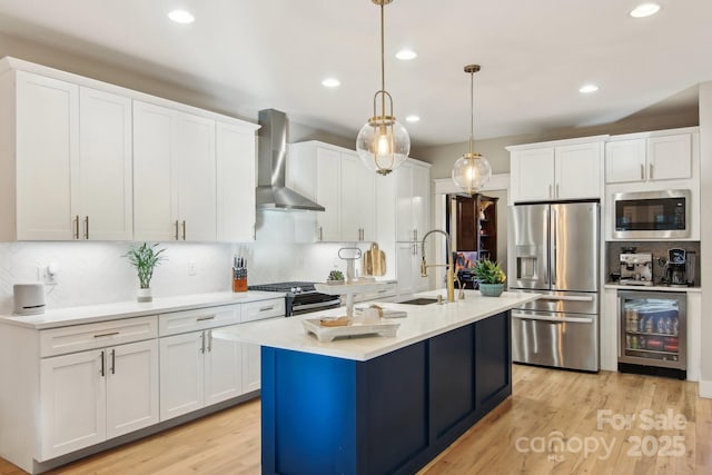 kitchen featuring wall chimney range hood, sink, stainless steel appliances, white cabinets, and beverage cooler