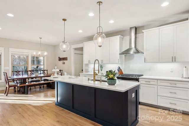 kitchen with decorative light fixtures, white cabinetry, sink, a center island with sink, and wall chimney exhaust hood