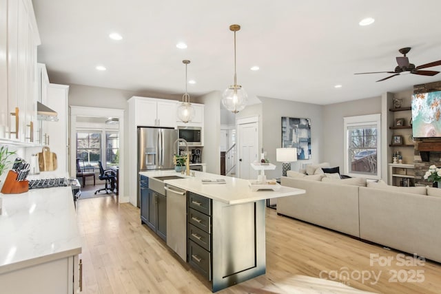 kitchen with stainless steel appliances, a center island with sink, white cabinets, and decorative light fixtures