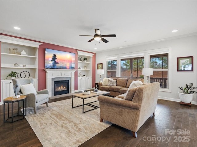 living room with built in shelves, ceiling fan, ornamental molding, and dark hardwood / wood-style flooring