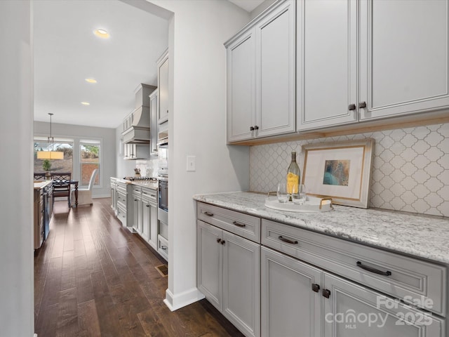 kitchen with decorative light fixtures, appliances with stainless steel finishes, dark hardwood / wood-style floors, custom range hood, and light stone countertops