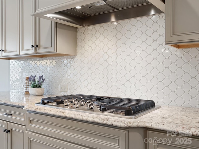 kitchen featuring light stone counters, stainless steel gas stovetop, backsplash, and wall chimney range hood