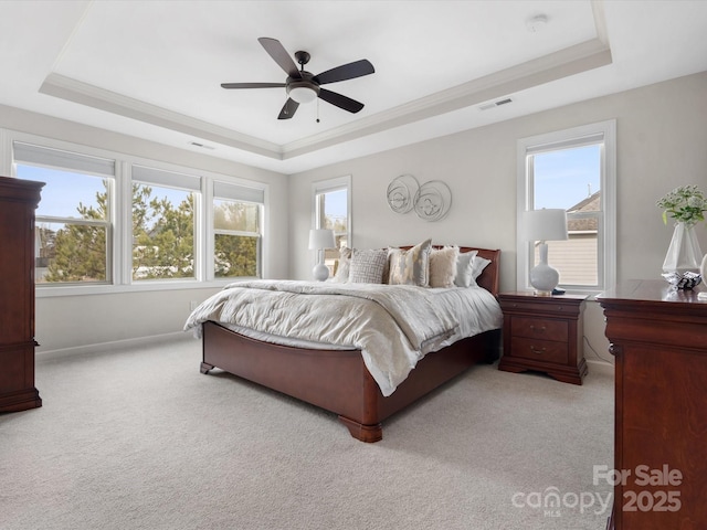 carpeted bedroom with ornamental molding, a tray ceiling, and multiple windows