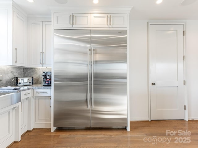 kitchen featuring built in refrigerator, white cabinetry, backsplash, and light hardwood / wood-style floors