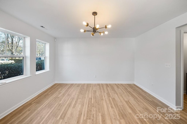 empty room featuring a chandelier and light wood-type flooring